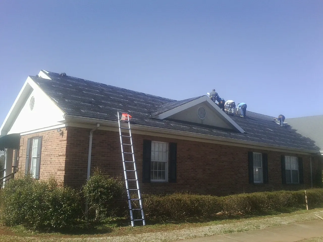 Crew tearing shingles off a brick ranch roof with a ladder set — Emergency Roof Repair work by our crew in Delhi