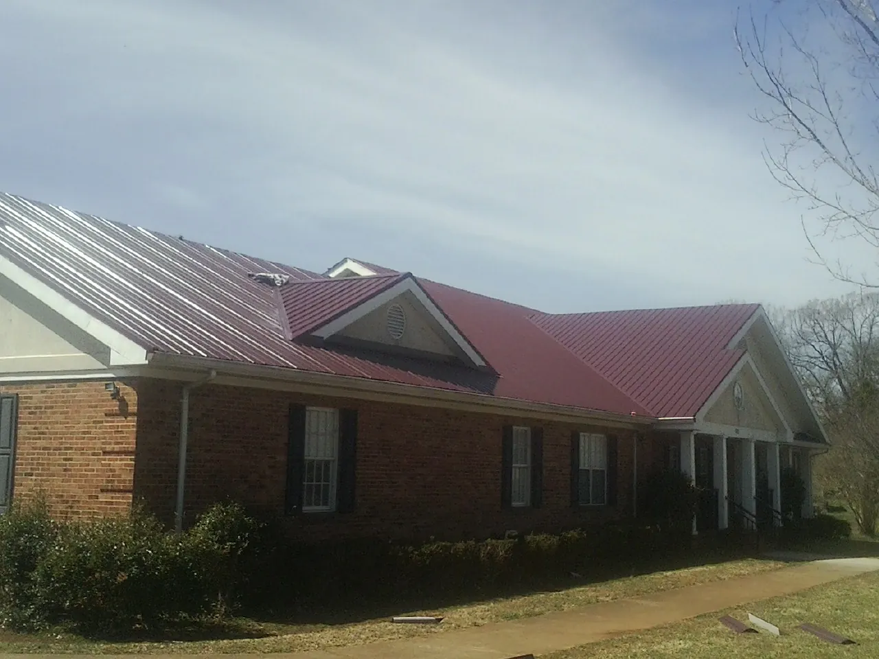 Red metal roof with gabled entries on a long brick building, from a Hail Damage Roof Repair job in Delhi