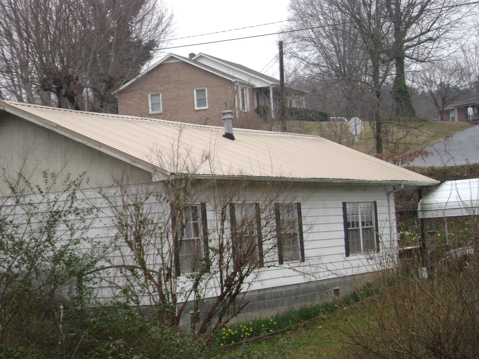 Tan metal roof on a white sided house set into a hillside — Commercial Roofing by Roofing Brothers in Delhi